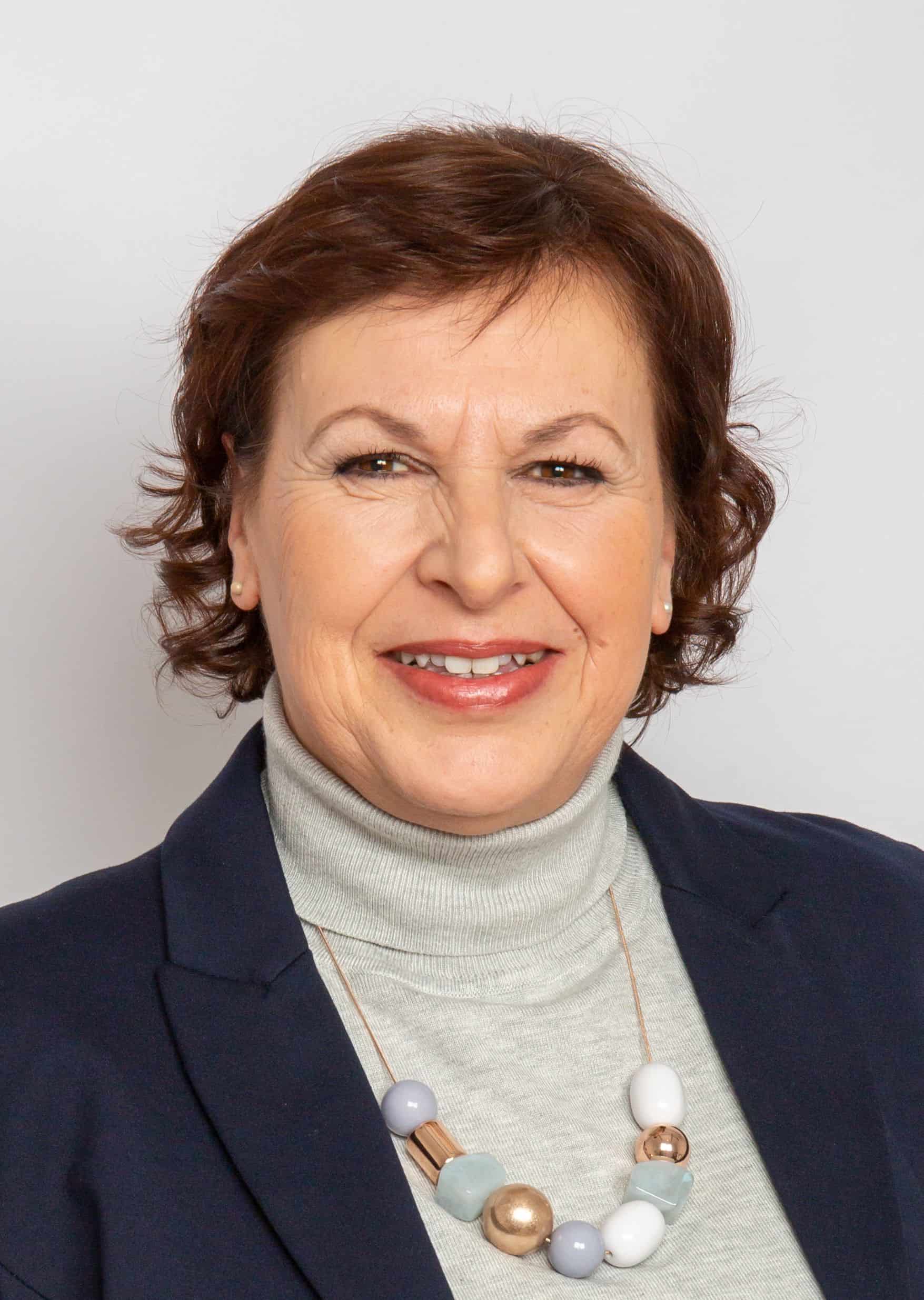 Porträt einer Frau mit Kurzhaarfrisur, Blazer und freundlichem Lächeln.