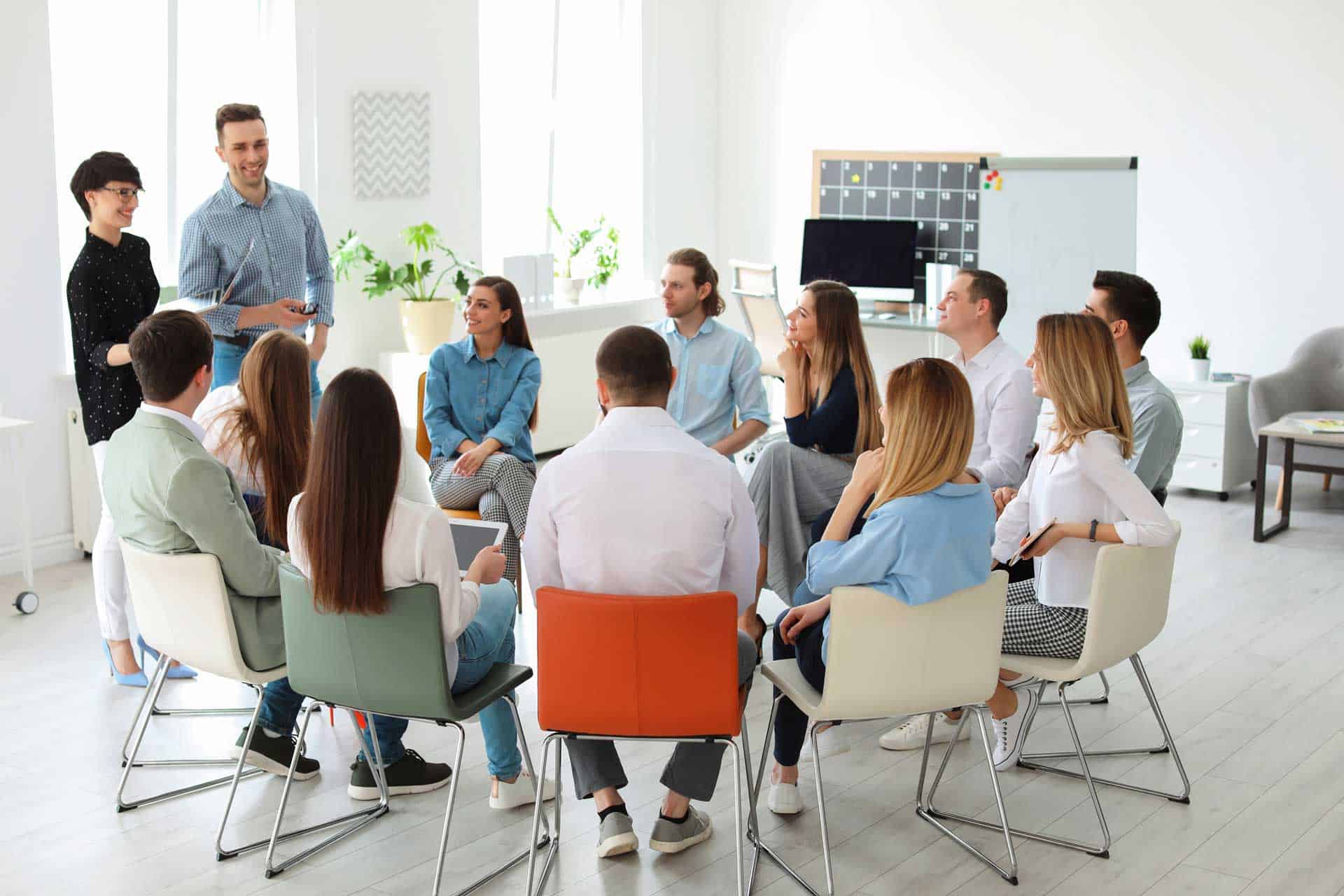 Teammeeting im hellen Büro mit 15 Personen, Diskussion und Zusammenarbeit.