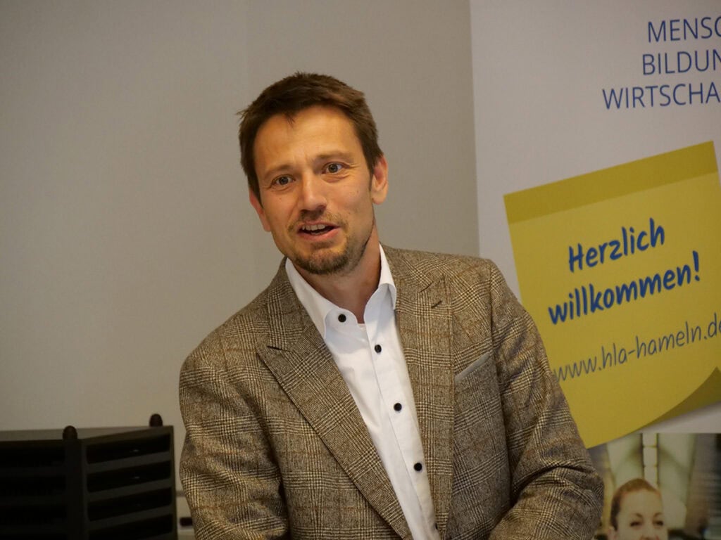 Mann spricht bei VLWN-Veranstaltung, Hintergrund mit Begrüßungsschild.