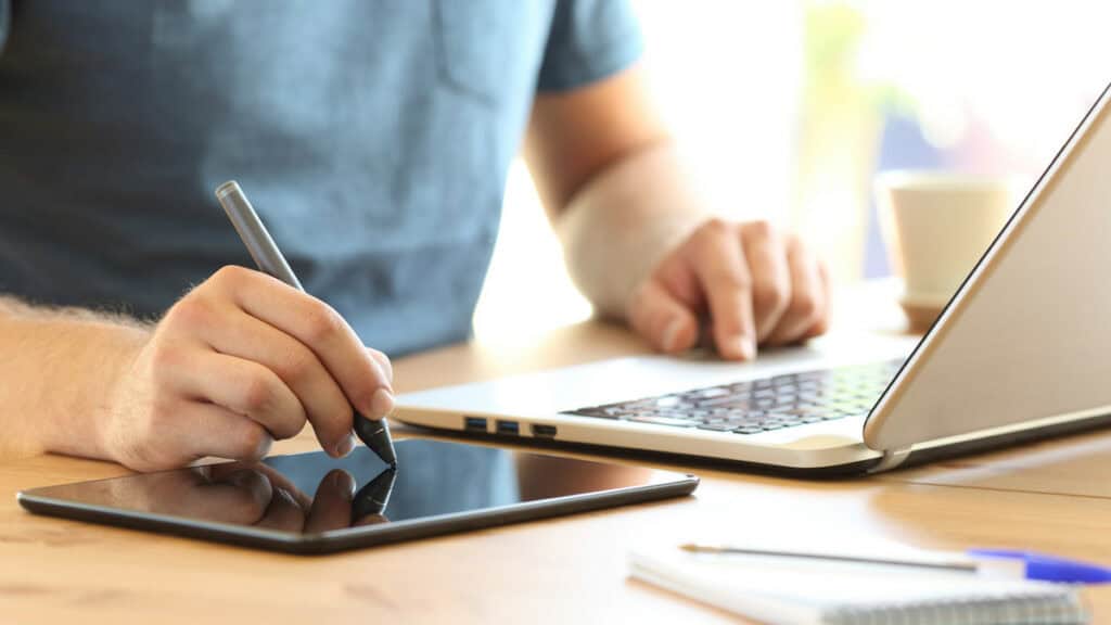 Person arbeitet mit Grafiktablett und Laptop für ganzheitlichen Arbeitsvorgang.