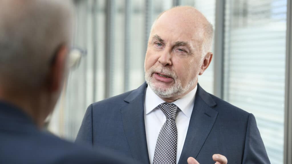 Älterer Mann im Anzug spricht ernsthaft mit einem jüngeren Mann in einem Büro.