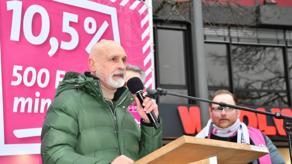 Mann bei Warnstreik in Aachen spricht vor Publikum mit Mikrofon.