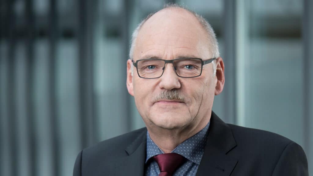 Mann in Anzug und Brille vor modernem Bürogebäude.