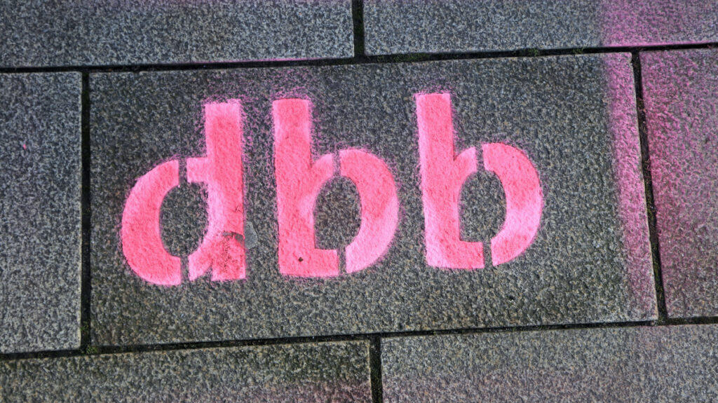 Pinke Graffiti "dbb" auf Gehwegplatten, symbolisiert Diskussionsthema.