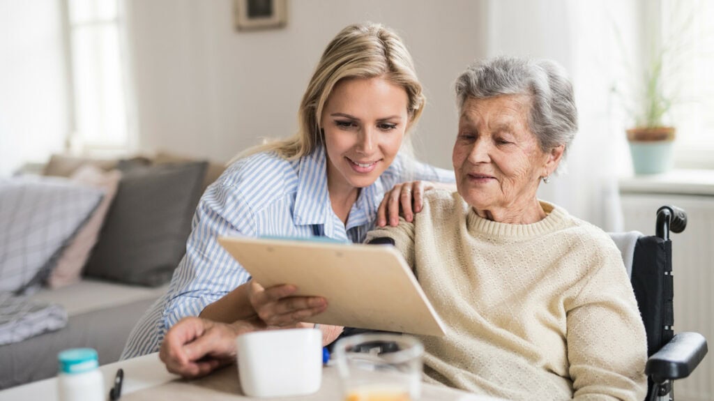 Pflegekraft unterstützt ältere Dame im Rollstuhl bei der Pflege zu Hause.
