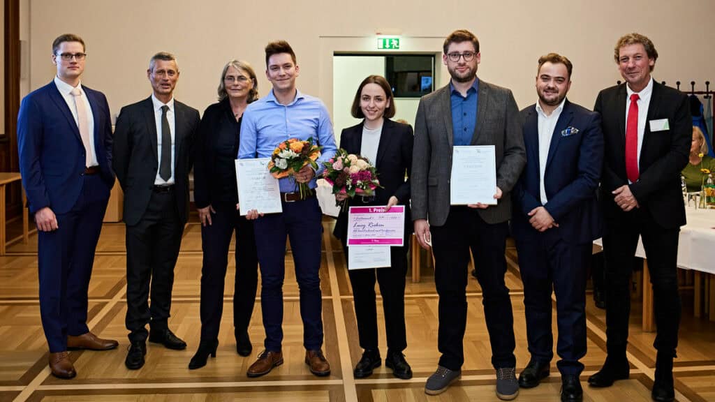 Gruppe junger Fachkräfte bei Preisverleihung für Abschlussarbeiten, feierliche Atmosphäre.