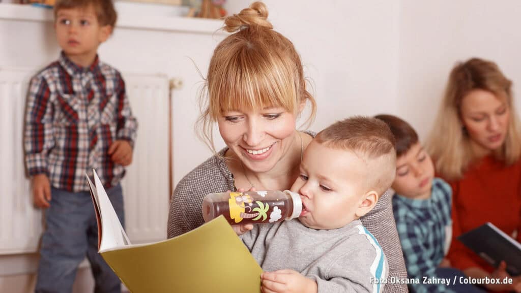 Frau mit Kind beim Trinken in einer Kita, lachend und glücklich.