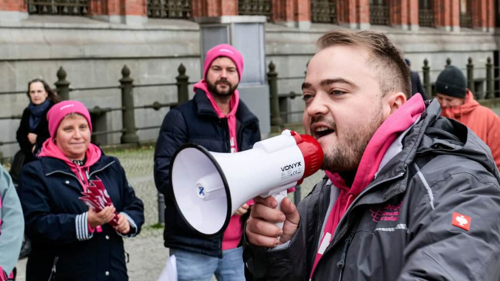 Mann mit Megafon bei einer Demonstration für Nachwuchsförderung im öffentlichen Dienst.