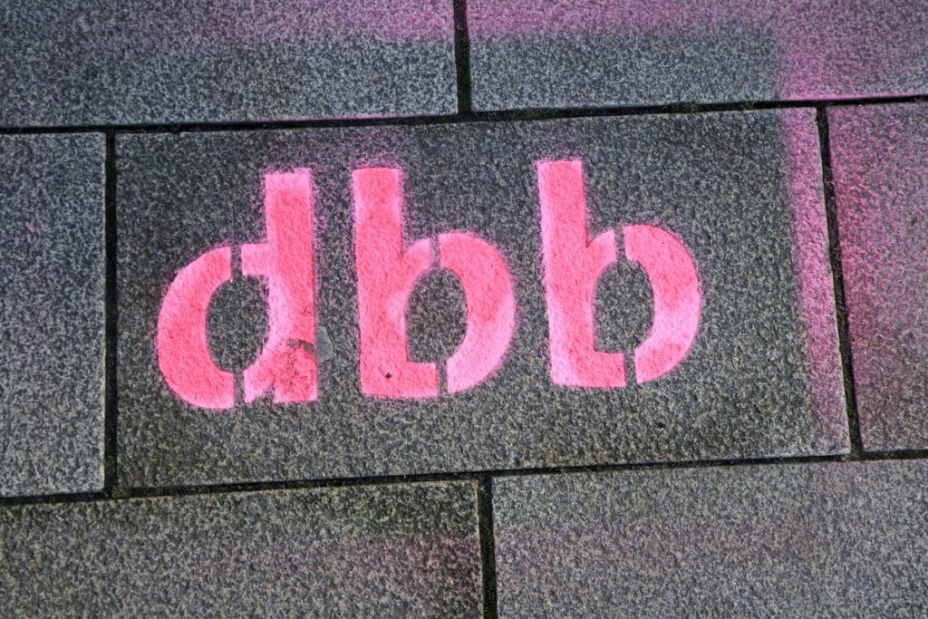 Graffiti mit "dbb" auf Gehwegplatten, symbolisiert Unterstützung der Bundesbeihilfe.