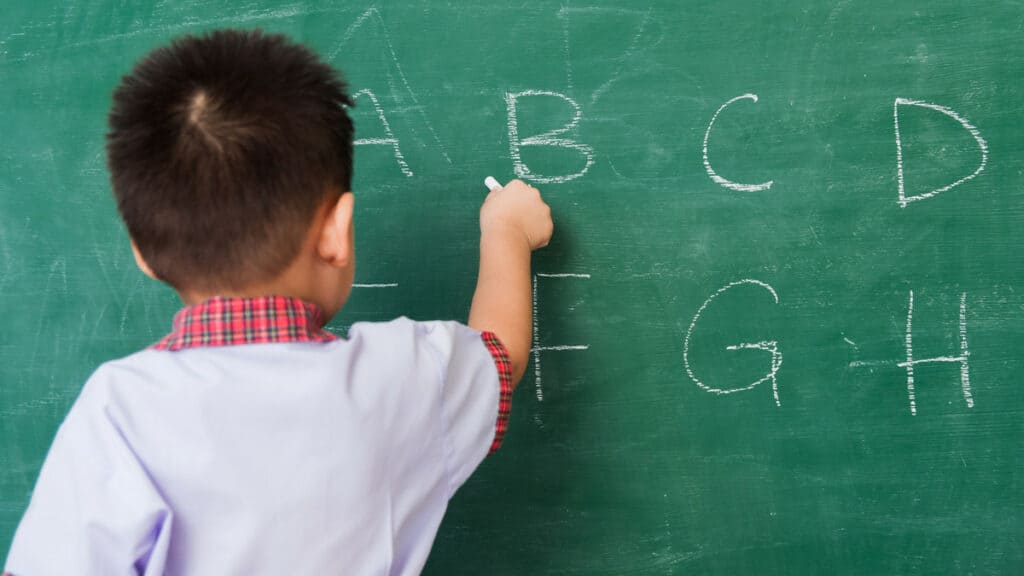 Junge Schülerin schreibt Buchstaben an die Tafel im Klassenzimmer.