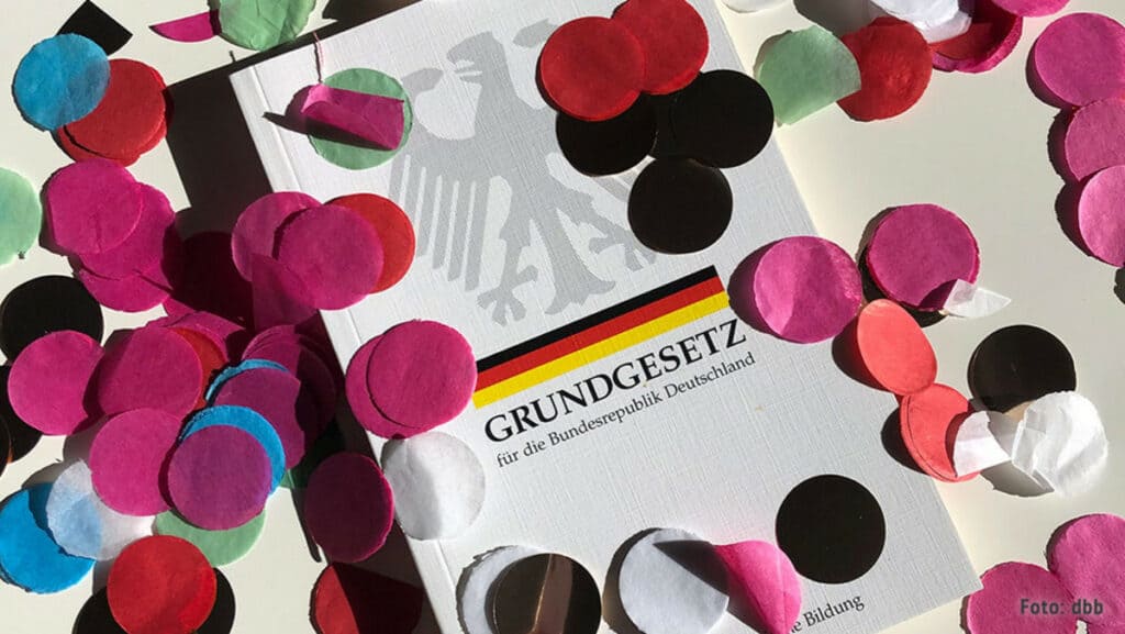 Grundgesetz-Broschüre umgeben von bunten Konfetti, symbolisiert politische Vielfalt.