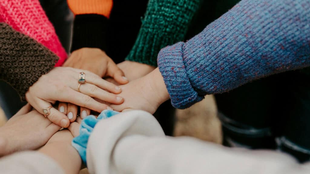 Mehrere Hände verschiedener Menschen greifen sich in der Mitte zusammen.