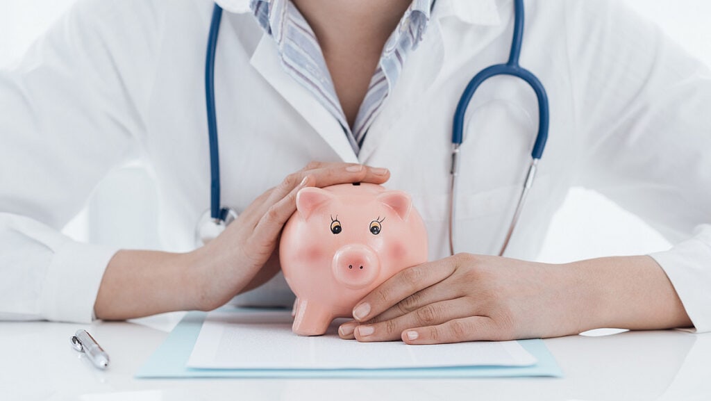 Arzt hält ein Sparschwein, symbolisiert Finanzplanung und Versicherung.
