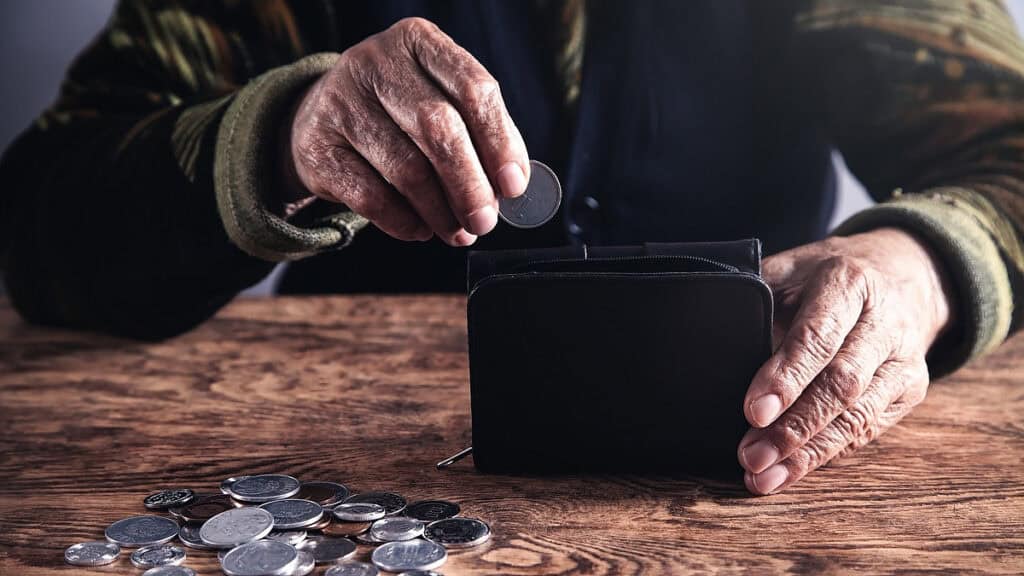 Ältere Person wirft Münze in Sparschwein, Symbol für Altersarmut.