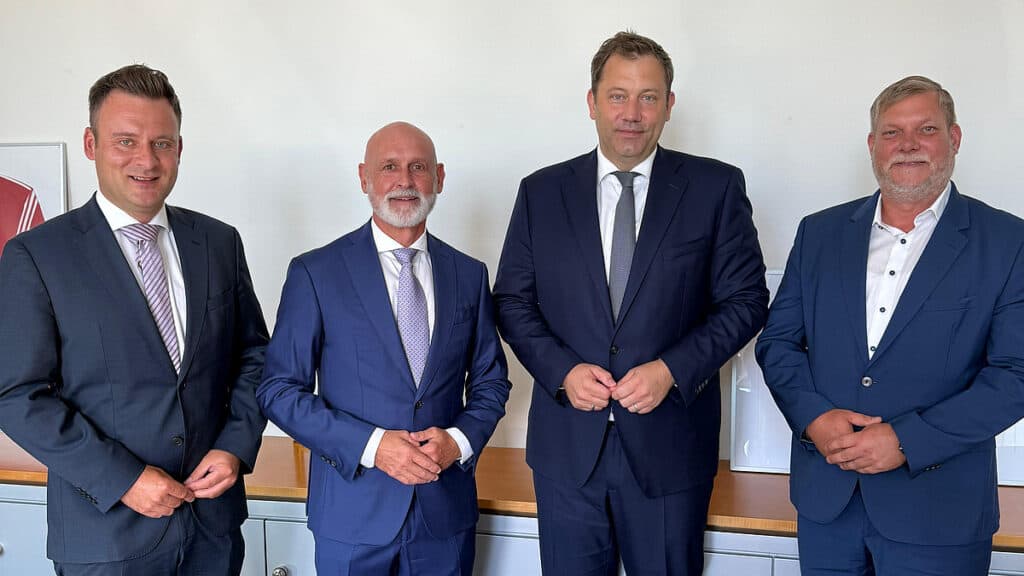 Vier Männer in Anzügen bei einer Besprechung im Büro.