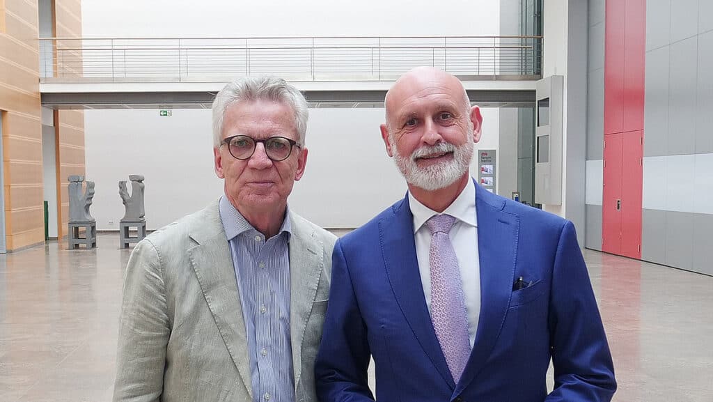 Zwei Männer in Anzügen bei einer Veranstaltung, Geyer spricht über Reformen.