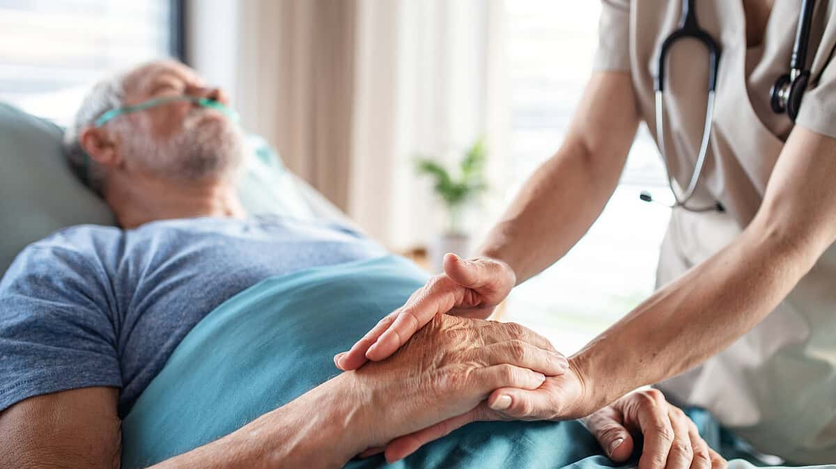 Pflegekraft berührt Hand eines älteren Patienten im Krankenhaus.