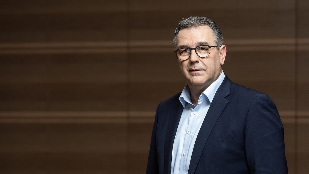 Mann in Anzug vor Holzwand, symbolisiert Ablehnung längerer Arbeitszeit.