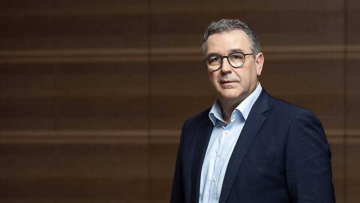 Mann in Anzug vor Holzwand, symbolisiert Ablehnung längerer Arbeitszeit.