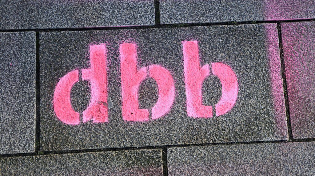 Graffiti mit "dbb" auf Gehwegplatten, symbolisiert Arbeitsbedingungen.