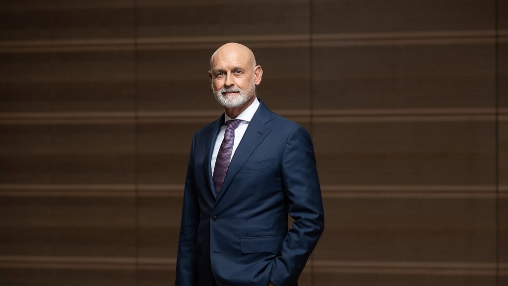 Politiker in Anzug vor Holzwand, symbolisiert staatliche Handlungsfähigkeit.