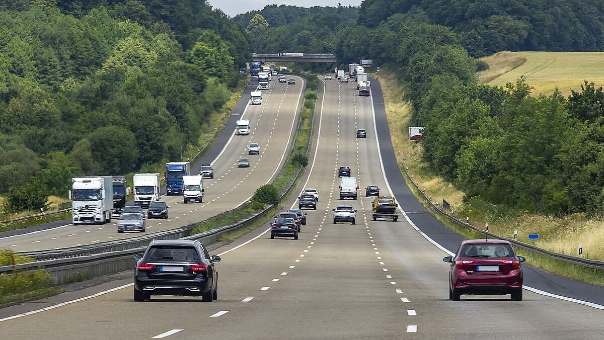 Autobahn mit mehreren Fahrzeugen im dichten Verkehr, umgeben von grüner Natur, symbolisiert Herausfo.