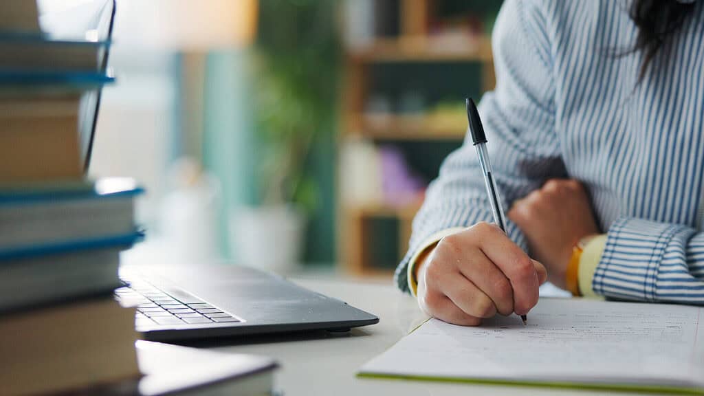 Person schreibt bei Schreibwettbewerb in einem Büro, Fokus auf Hand und Stift.