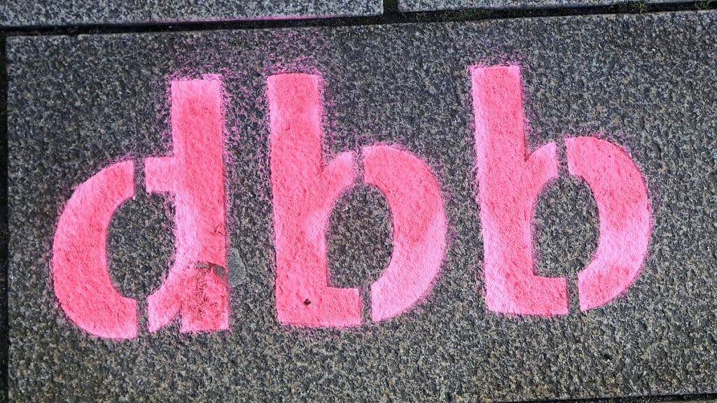Graffiti mit pinken Buchstaben "d b b" auf dunklem Hintergrund.